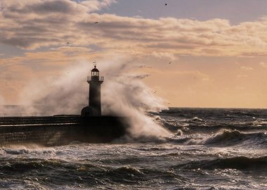 Wave against lighthouse of Porto, Portugal, in the sunset light clipart