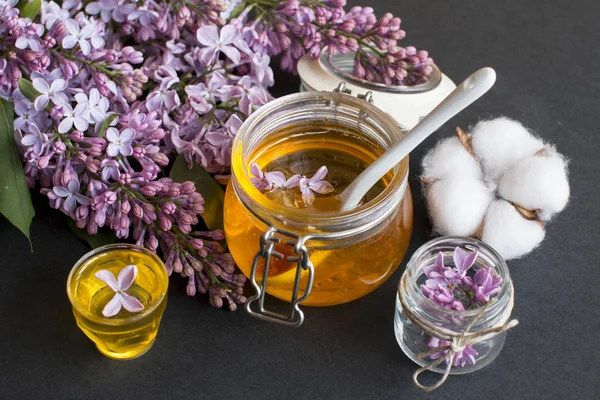 a jar of fragrant flower honey. Honey saved and lilac flowers. On black and wooden background.