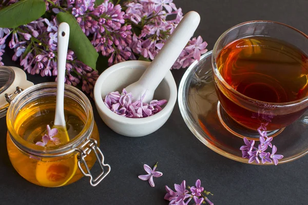a jar of fragrant flower honey. Honey saved and lilac flowers. Cup of black tea.