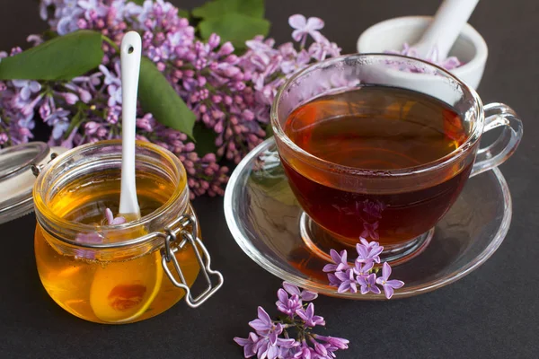 a jar of fragrant flower honey. Honey saved and lilac flowers. Cup of black tea.