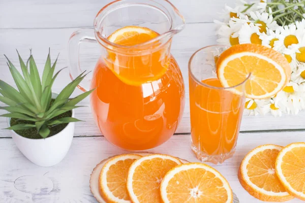 Orange vitamin drink. Decanter and glass with orange drink decorated with white daisies.