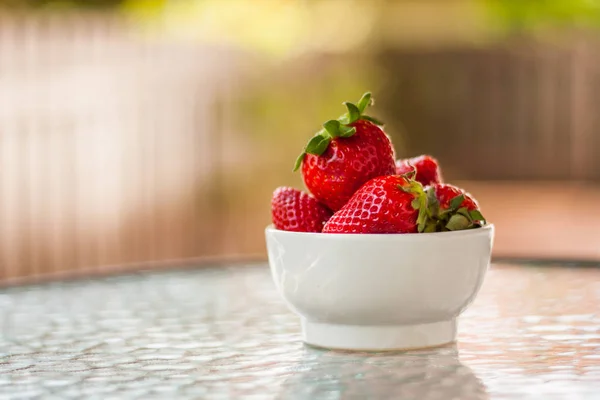 Taze ve tatlı olgun kırmızı çilek İspanya'dan bir masada koyu ahşap açık havada. Sağlıklı yiyecek ya da tatlı bir küçük beyaz seramik kase bir olarak hizmet.