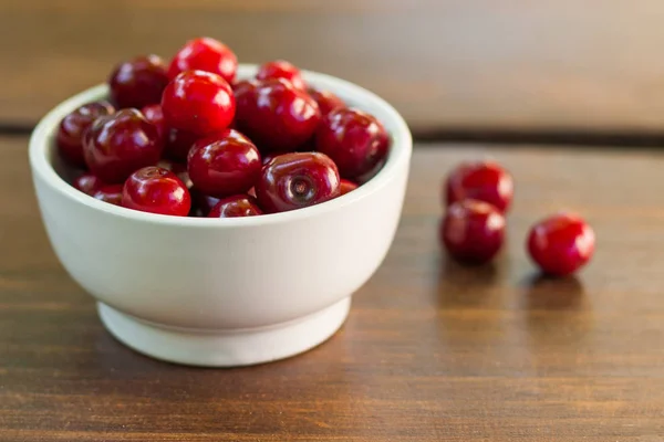 Parlak kırmızı olgun taze erken tatlı kiraz aldım koyu ahşap bir masa üzerinde olabilir. Bir kalp - aşk sembolü şekli oluşturan tek kiraz saplarını bir beyaz seramik kase ile meyve.