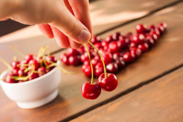 Parlak kırmızı olgun taze erken tatlı kiraz aldım koyu ahşap bir masa üzerinde olabilir. Bir kalp - aşk sembolü şekli oluşturan tek kiraz saplarını bir beyaz seramik kase ile meyve.