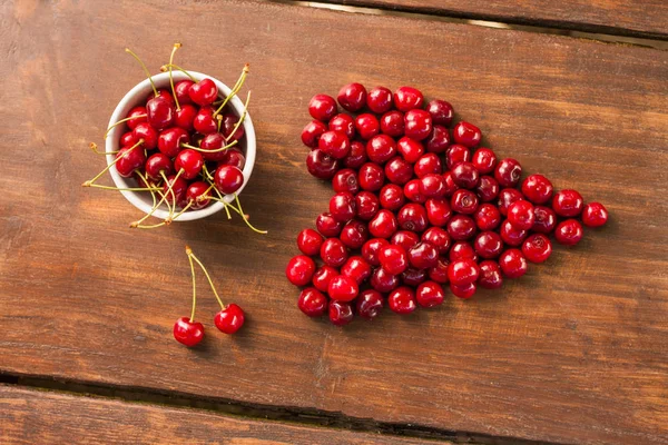 Parlak kırmızı olgun taze erken tatlı kiraz aldım koyu ahşap bir masa üzerinde olabilir. Bir kalp - aşk sembolü şekli oluşturan tek kiraz saplarını bir beyaz seramik kase ile meyve.