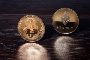 Bir koyu ahşap yüzeye yansıtıldığı altın Bitcoin ve ethereum kripto para birimi fiziksel gerçek metal paraları.