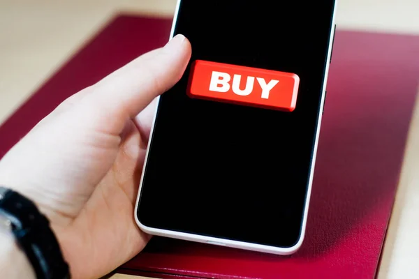 Buy button on a phone screen. Bright red buy button on a black phone screen, holding in hand. Making money on your smartphone.