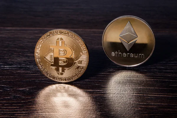 Bir koyu ahşap yüzeye yansıtıldığı altın Bitcoin ve ethereum kripto para birimi fiziksel gerçek metal paraları.