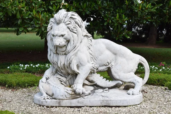 White statue with lion attacking a crocodile with green background of garden