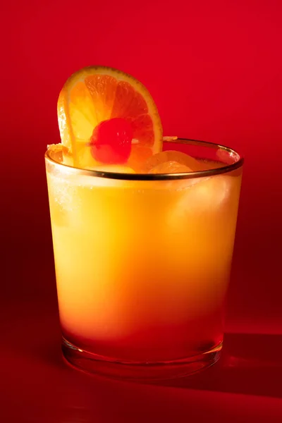 Tequila sunrise in a glass with golden rim garnished with orange slice and cherry