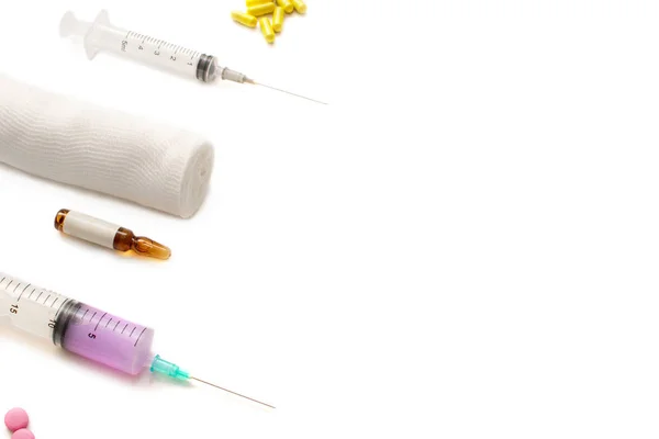 Pink and yellow pills, medical syringe for injections, ampoules and a bandage on a white background