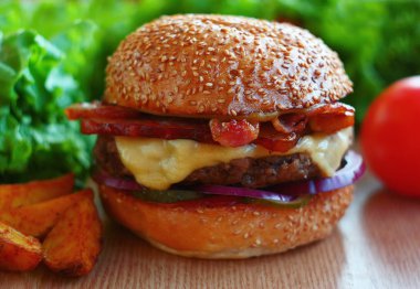 Sığır eti, peynir, jambon, turşu, soğan ile sulu hamburger. Masaya arasında taze sebze ve patates kızartması