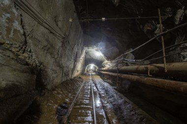 Yeraltı altın madeni tüneli raylar ve ışık ile sürükleniyor.