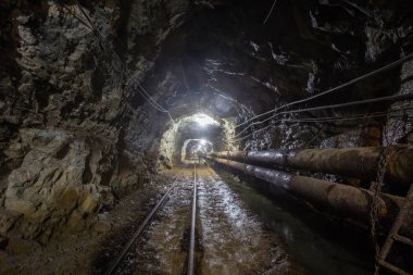 Yeraltı altın madeni tüneli raylar ve ışık ile sürükleniyor.
