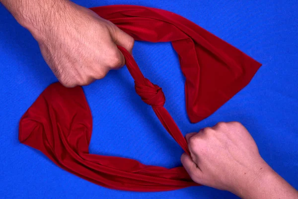 Erkek ve kadın eli mavi bir arka planda kırmızı bir eşarp çekiyor.