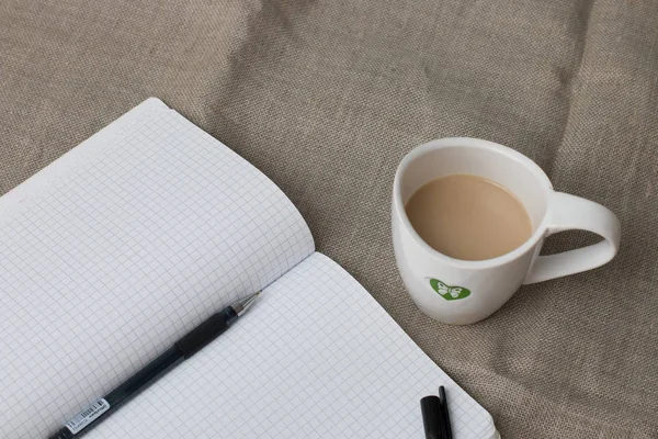 chechered clean notebook with pen and cup of coffee on the flax background on the table