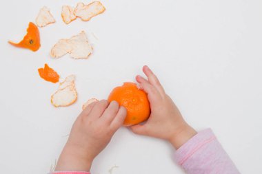 çocuk elleri beyaz bir arka plan pembe turuncu üzerinde mandalina soyma
