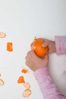 çocuk elleri beyaz bir arka plan pembe turuncu üzerinde mandalina soyma