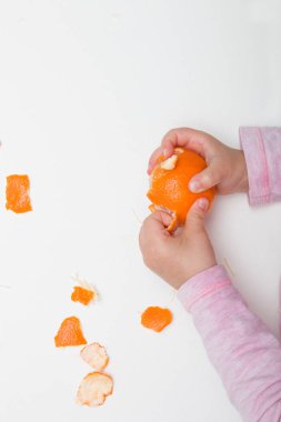 çocuk elleri beyaz bir arka plan pembe turuncu üzerinde mandalina soyma