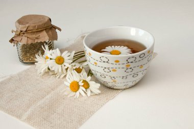 kavanoz, beyaz bir masa izolasyon natürmort üzerinde bej kumaş ve papatya çiçekleri üzerinde çay fincan