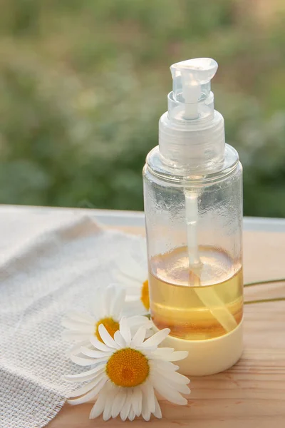 natural cosmetics natural care oil in a bottle on the window place copy daisy green background white flower wooden board