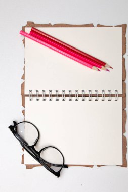 beyaz masa arka plan pembe kırmızı renkli kalemler üzerinde temiz bir defter sayfalarında gözlük
