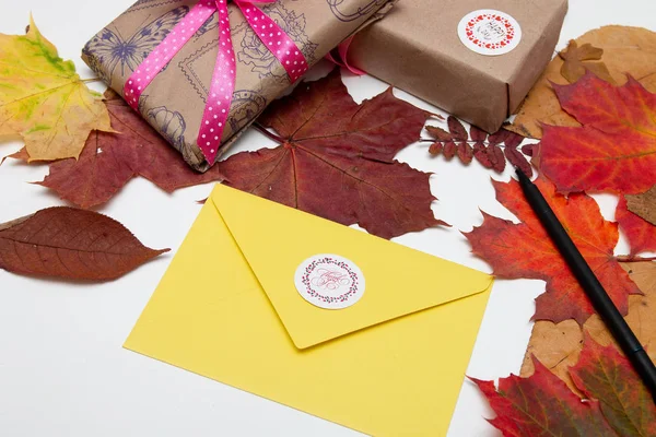 Thanksgiving background, yellow envelope with the inscription thank you, gifts with beautiful ribbons, maple autumn leaves on a white table, copy space, flat lay, top view, thanksgiving, holiday