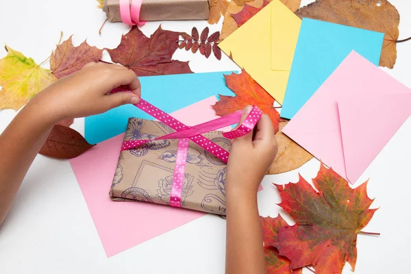 çocuk el şükran mevcut pembe bir kurdele yay bağlar, hediyeler kutuları, zarflar ve beyaz bir masa üzerinde sonbahar yaprakları, kopya alanı, üst görünümü