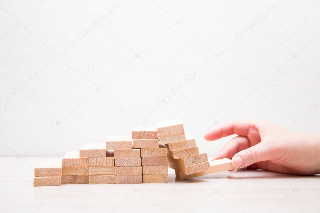Hand pulls out part of the foundation of a staircase from wooden dominoes, business concept, business fall