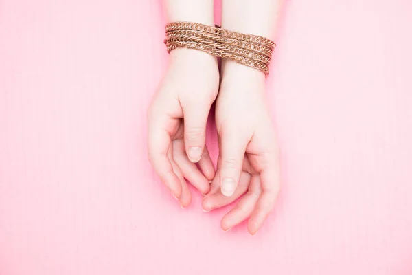female hands chained in a gold chain on a pink background, domestic violence