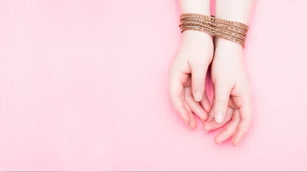 female hands chained in a gold chain on a pink background, domestic violence