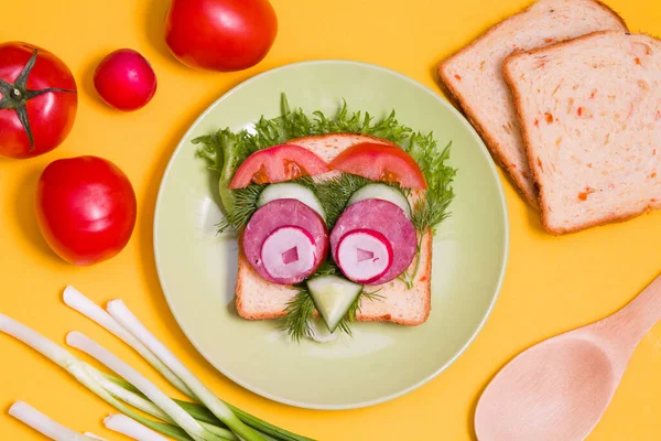 緑のプレートにかわいいサンドイッチ 黄色の背景にパン トップビュー 子供のための面白い朝食 フクロウ型のサンドイッチ ソーセージマグカップ — ストック写真