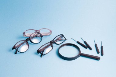Bir büyüteç, birkaç çift gözlük ve küçük tornavida mavi arka planda, yetişkinler için çocuk gözlüğü ve gözlükleri tamir ediliyor