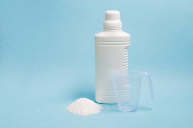 Etiketsiz yıkama için sıvı jel ve yanında toz bulunan bir ölçü kabı, mavi arka plan fotokopi alanı.