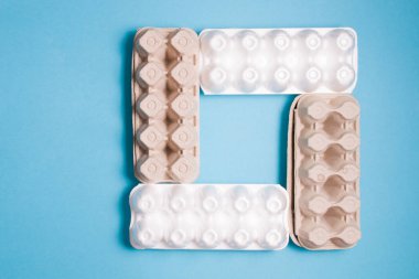 Yumurtalar için çeşitli kutular mavi arka planda bir kareye yerleştirilmiştir. Kopya alanı, üst görünüm, polistiren ve kartondan yapılmış yumurtalar için ambalaj.