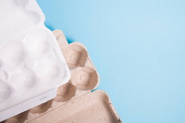 Mavi arkaplandaki yumurtalar için karton ve köpük kutular, kopyalama alanı, üst görünüm, yumurta için farklı ambalaj, plastik kirliliği kavramı