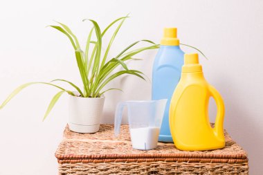Ölçüm kabında çamaşır tozu, tencerede bitki, parlak plastik şişelerde jel ve kumaş yumuşatıcısı hasır bir fırçada, renkli giysileri yıkama konsepti