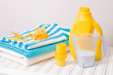 Renkli çamaşır yığını, mandallar, ölçü kabında çamaşır deterjanı ve kirli çamaşırları yıkamak için beyaz plastik bir sepette sarı bir şişede çamaşır jeli.