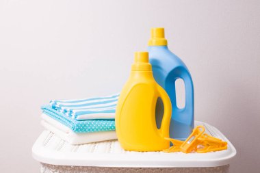 Bir yığın renkli çamaşır, kurutma kıskaçları ve jelleri kirli çamaşırları yıkamak için beyaz plastik bir sepete koyup sarı ve mavi şişelerle yıkamak.