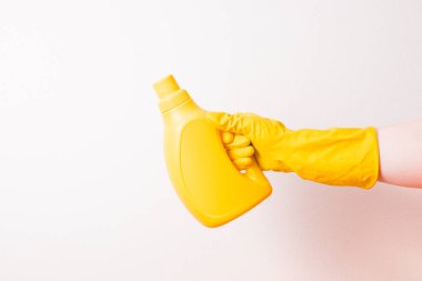 Sarı kauçuk eldivenli bir kadın eli, arka planda etiket olmayan sarı bir çamaşır jeli tutar. Kopya spac
