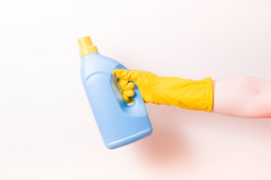 Sarı kauçuk eldivenli bir kadın eli açık mavi bir çamaşır jeli tutuyor. Üzerinde sarı bir başlık var. Üzerinde etiket yok.