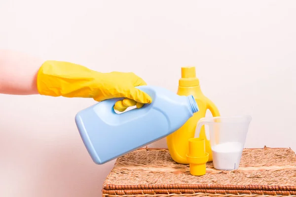 woman in yellow rubber gloves pours a softener for kids clothes in little yellow cup for washing liquid