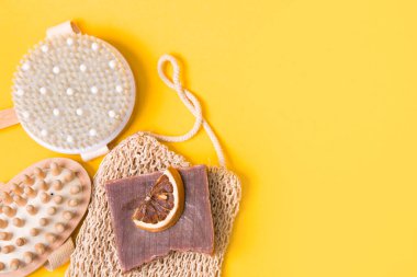 kuru anti-selülit masaj fırçası, örülmüş bez, ev yapımı kakao sabunu, kurutulmuş portakal dilimleri ve sarı arka planda ahşap vücut masajı, üst manzara, kopyalama alanı, düz yatış
