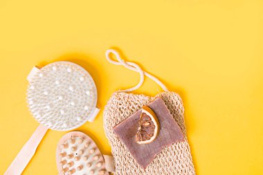 kuru anti-selülit masaj fırçası, örülmüş bez, ev yapımı kakao sabunu, kurutulmuş portakal dilimleri ve sarı arka planda ahşap vücut masajı, üst manzara, kopyalama alanı, düz yatış