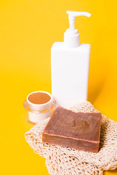 jar of ground coffee, a knitted washcloth, homemade cocoa soap,, a white bottle with a dispenser without a label on a yellow background, body care at home