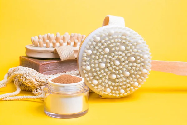 jar of ground coffee, brush for dry anti-cellulite massage, a knitted washcloth, homemade cocoa soap, a wooden massager on a yellow background, close-up, home body care, zero waste lifestyle