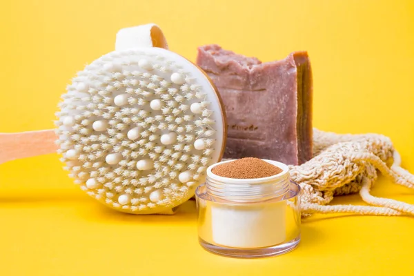 jar of ground coffee, a brush for dry anti-cellulite massage, a knitted washcloth, homemade cocoa soap on a yellow background, close-up, home body care, zero waste lifestyle concept