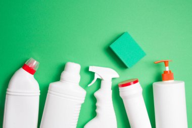 Yıkama için yeşil süngerler ve yeşil arka plandaki deterjanlar için etiketsiz çeşitli beyaz plastik şişeler fotokopi alanı