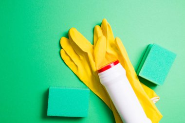 Temizlik için yeşil süngerler, sarı lastik eldivenler ve yeşil arka plandaki toz deterjanı için beyaz plastik şişe.