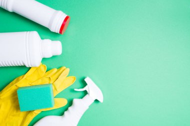 Sarı lastik eldivenler, yeşil süngerler ve yeşil arkaplan görünümlü deterjanlar için etiketsiz çeşitli beyaz plastik şişeler.